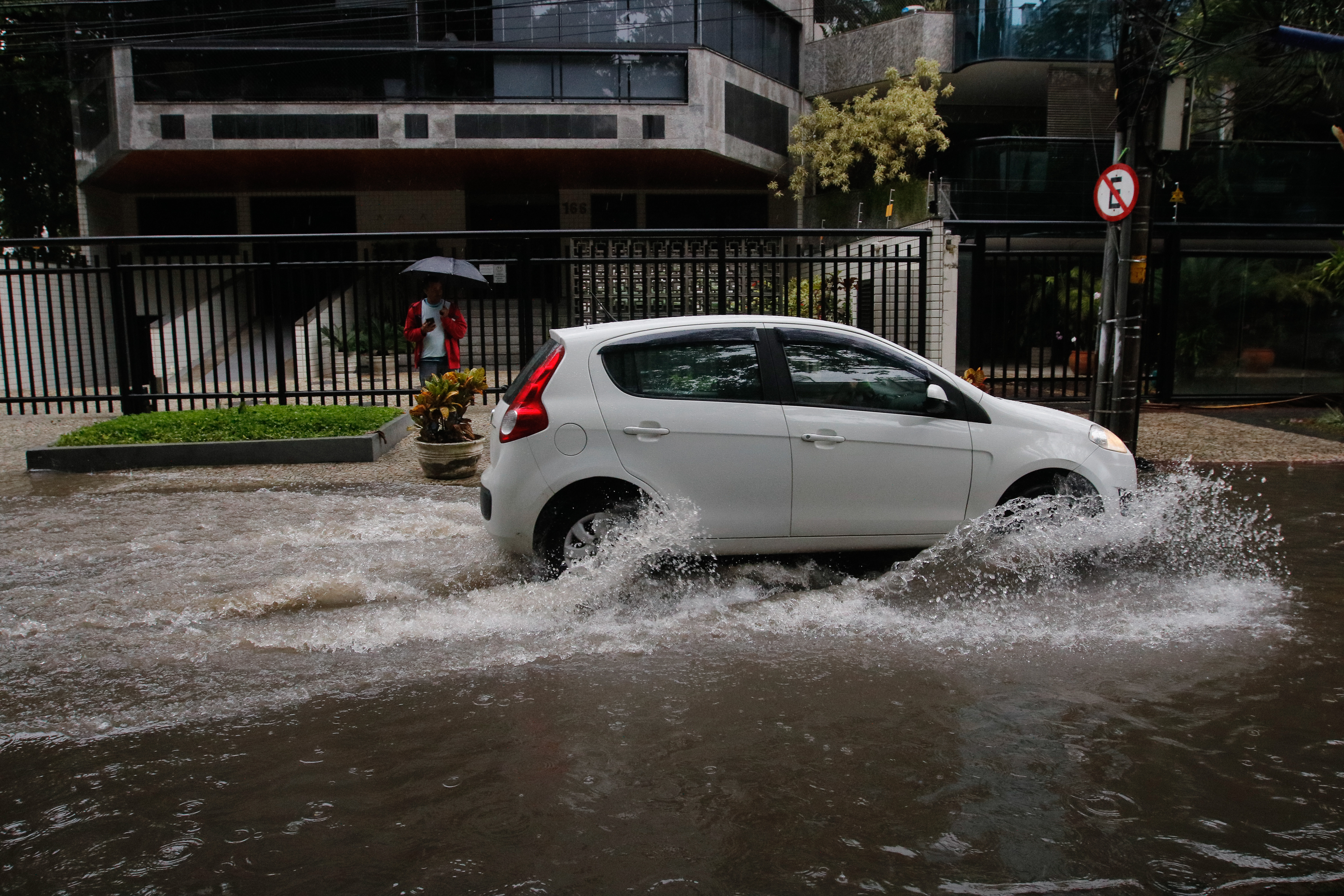 Rua alagada no Rio de Janeiro após temporal, com carros passando pela água
